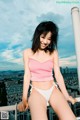 A woman in a pink top and white bikini posing on a balcony.