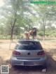 A woman leaning on the hood of a car in a park.