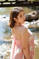 A woman in a pink dress standing by a river.